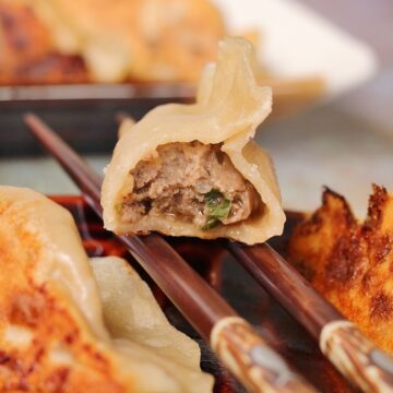 closeup of a half-eaten Chinese beef dumpling resting on two chopsticks over a plate