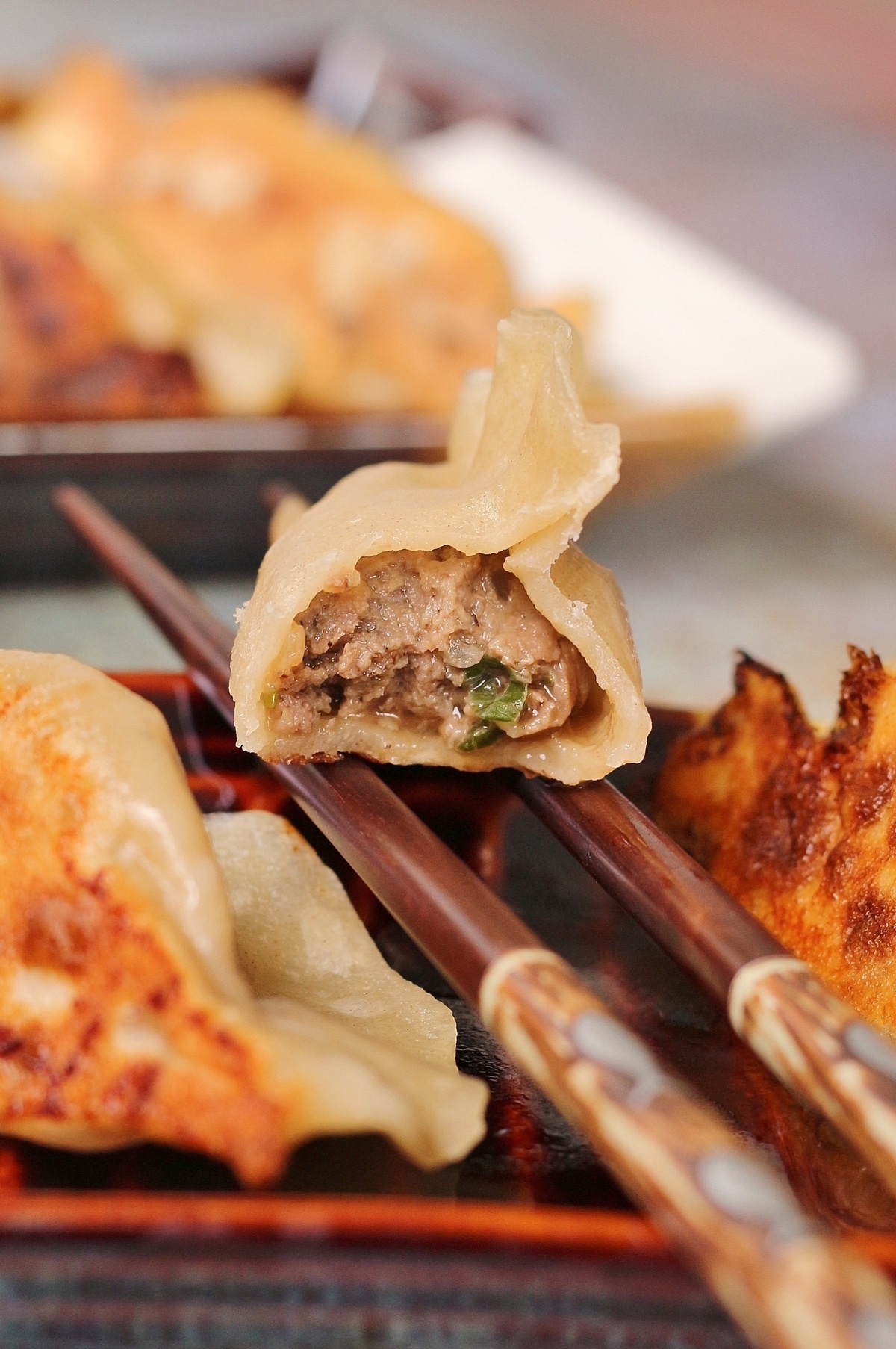 closeup of a half-eaten Chinese beef dumpling resting on two chopsticks over a plate