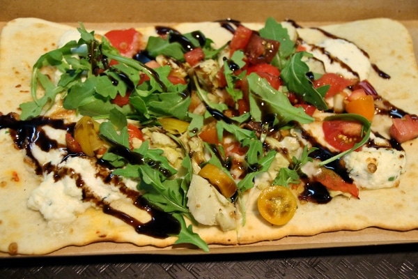 a flatbread pizza with cheese, cherry tomatoes, arugula, and balsamic