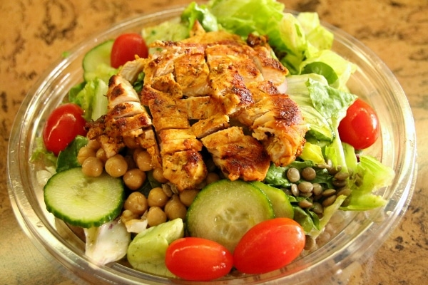 A plastic container filled salad and grilled chicken