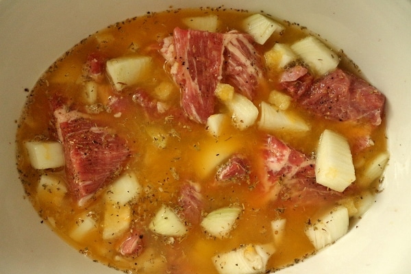 big cubes of pork with onions and liquid in a slow cooker