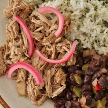 A plate of mojo pork with pickled onions, black beans, and rice