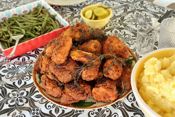 a big platter of fried chicken flanked by bowls of green beans and mashed potatoes