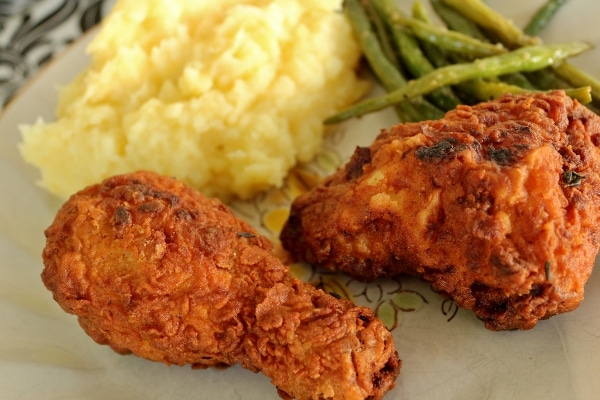 closeup of fried chicken on a plate with mashed potatoes and green beans