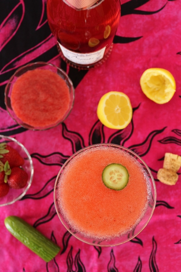 overhead view of a pink cocktail next to lemons and a bowl of strawberries