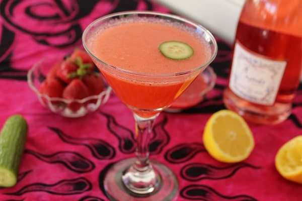 side view of a pink cocktail with a cucumber garnish