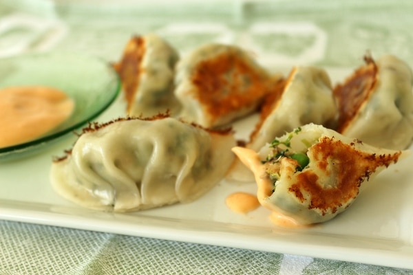 a plate of pan-fried dumplings with a bite taken out of one