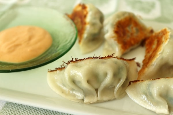 a plate of pan-fried dumplings with dipping sauce on the side