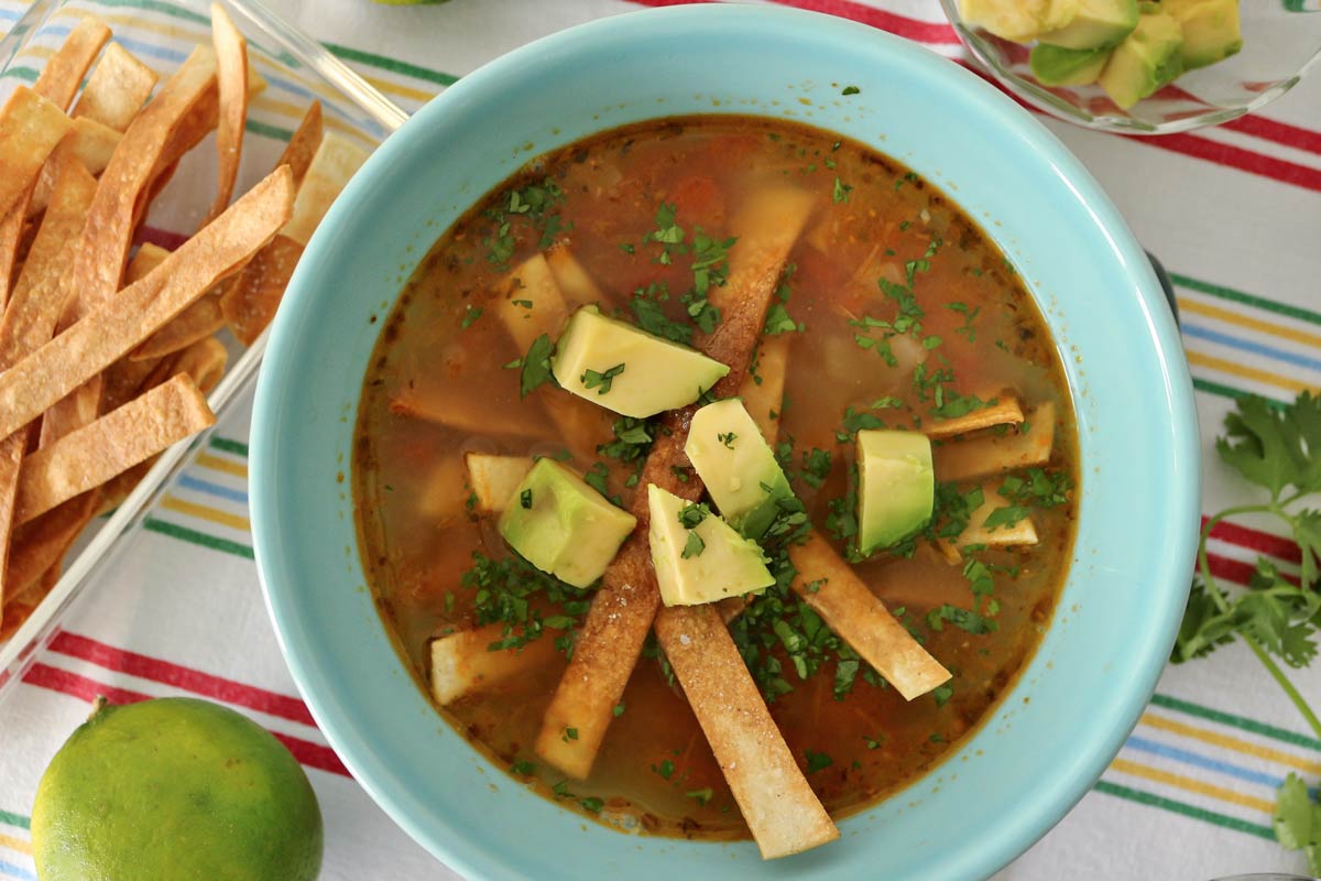 Soup topped with cubed avocado and fried tortilla strips in a blue bowl.