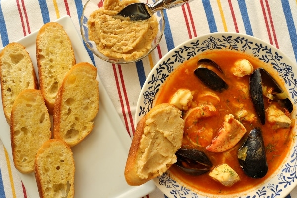 overhead view of a bowl of bouillabaisse with croutons and rouille on the side