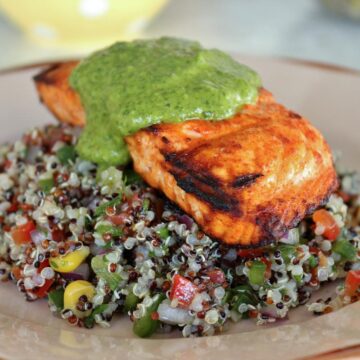 Grilled salmon over quinoa salad, topped with green sauce on an antique plate.