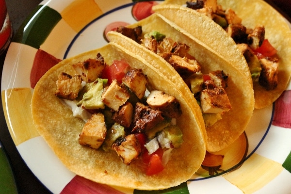 Three chicken tacos on corn tortillas, arranged on a colorful plate.