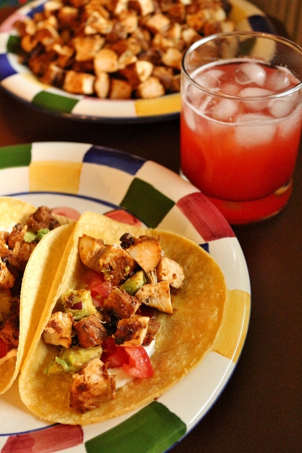 A plate of chicken tacos with a glass of strawberry agua fresca in the background