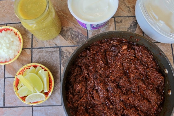 A skillet of shredded braised beef short ribs surrounded by toppings