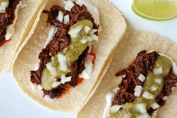 overhead view of braised short rib tacos with salsa verde and onions