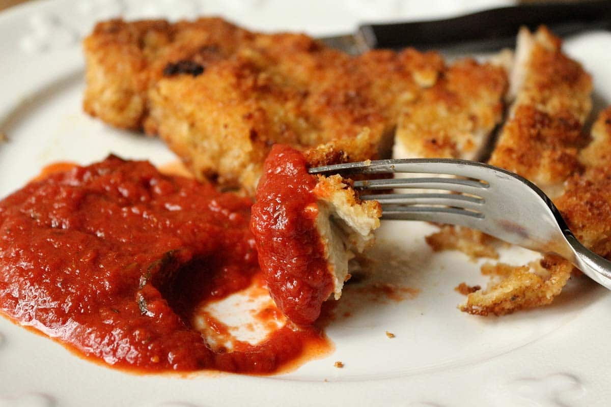 A piece of Milanese pork on a fork dipped in tomato sauce.