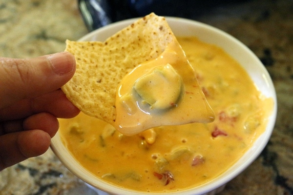 Tortilla chip dipped in homemade queso, showing off a piece of pickled jalapeno