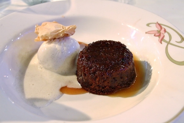 a sticky toffee pudding served with ice cream in a wide bowl