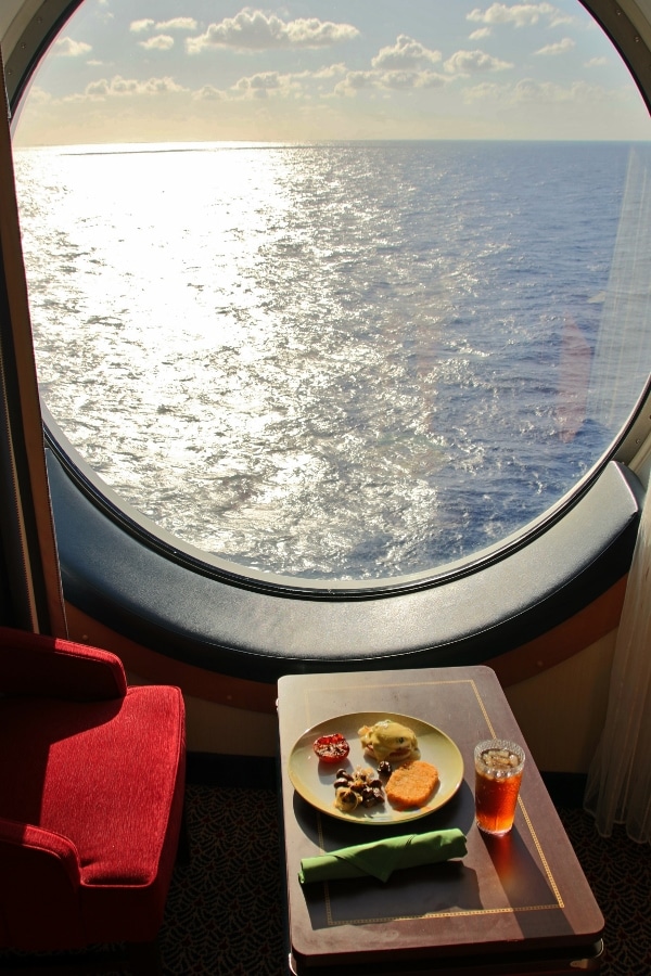 a plate of breakfast food on a small table next to a porthole overlooking the sea