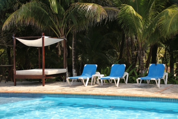 pool chairs and a canopied bed next to a pool and palm trees