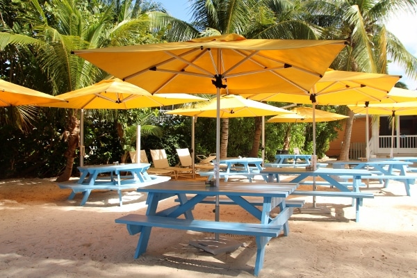 blue picnic tables covered with yellow umbrellas on a beach