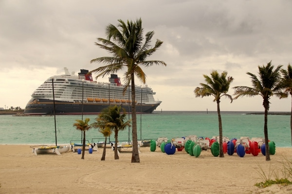 The Disney Fantasy cruise ship beyond a beach with palm trees and beach vehicles