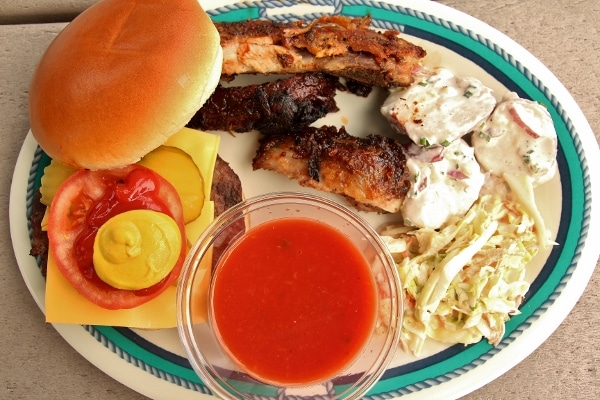 a burger, ribs, and salads on an oval plate