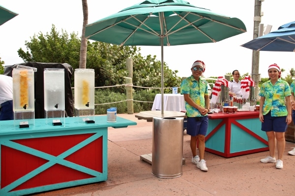 people posing near a group of water coolers under a beach umbrella