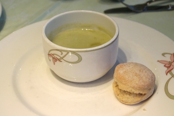 a cup of green soup with a small biscuit on the side