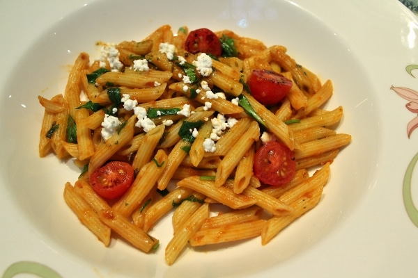 A plate of penne with tomatoes and crumbled cheese