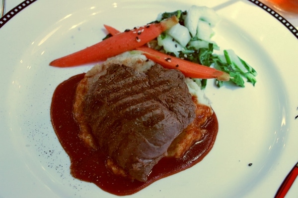 sliced steak served on a plate with vegetables and a dark brown sauce