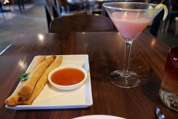 A plate of spring rolls next to a pink cocktail
