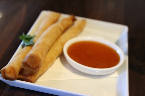 A close up of a plate of spring rolls with dipping sauce