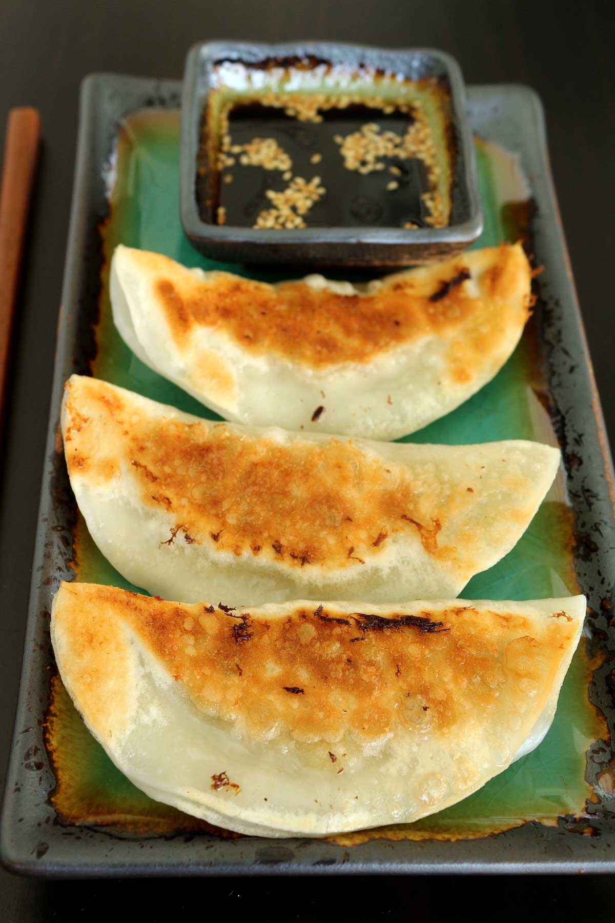 Closeup of pan-fried dumplings on a green rectangular plate.