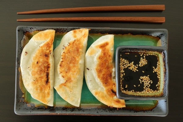 3 pan-fried dumplings on a plate with dipping sauce on the side