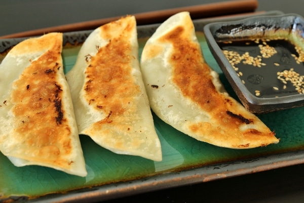 3 pan-fried dumplings on a plate with dipping sauce on the side