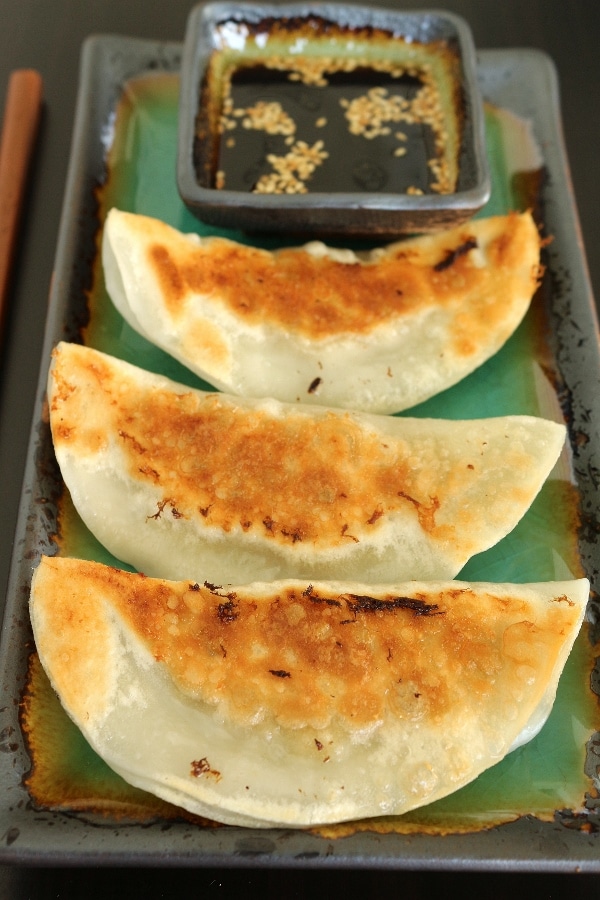 3 pan-fried dumplings on a plate with dipping sauce on the side