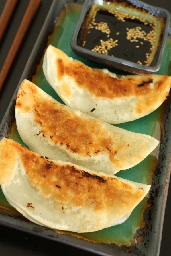 3 pan-fried dumplings on a plate with dipping sauce on the side