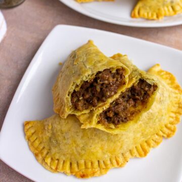 A Jamaican patty broken in half, resting on top of another patty on a white plate.