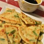 A close up of a plate of Korean scallion pancakes with dipping sauce