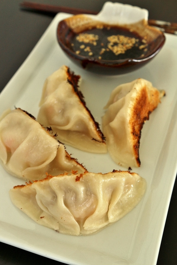 4 pan-fried dumplings on a rectangular plate with dipping sauce