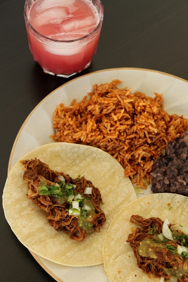 braised chicken tacos with rice and refried beans, and a glass of agua fresca