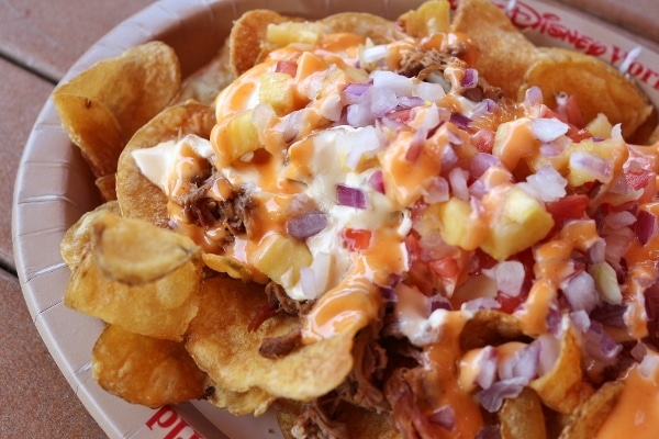 A close up of nachos with pulled pork, pineapple, and red onion