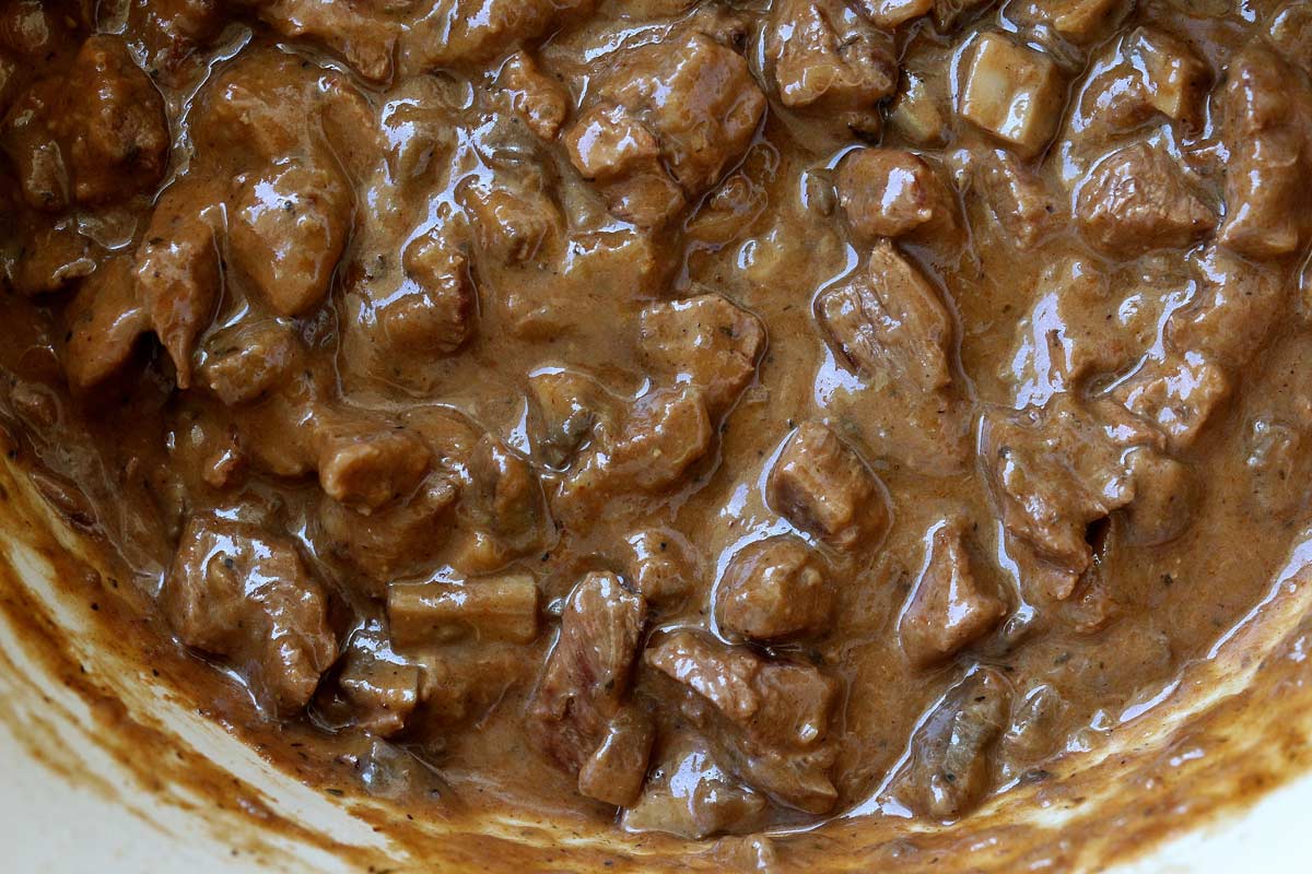 Thick beef and mushroom stew with brown sauce in an enameled cast iron pot.