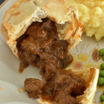 A small pie broken open on a plate with beef and mushroom filling spilling out.