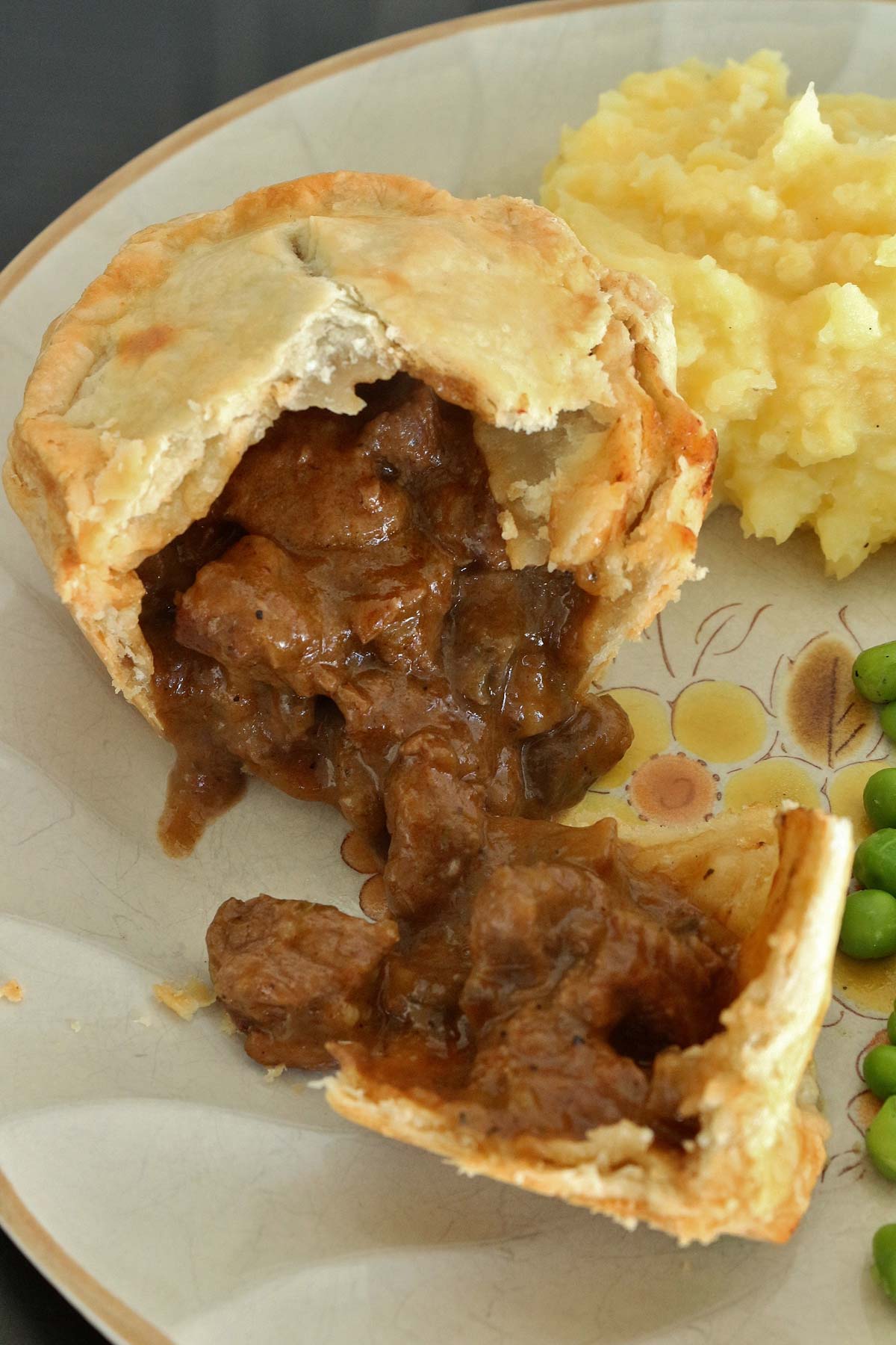 A small pie broken open on a plate with beef and mushroom filling spilling out.