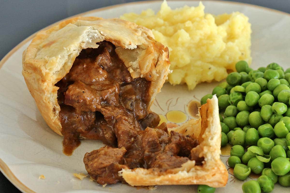 Closeup of an individual beef and mushroom pie broken open on a rustic plate.
