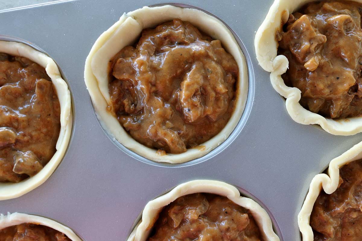 Closeup of a jumbo muffin pan lined with pastry dough and filled with beef stew.