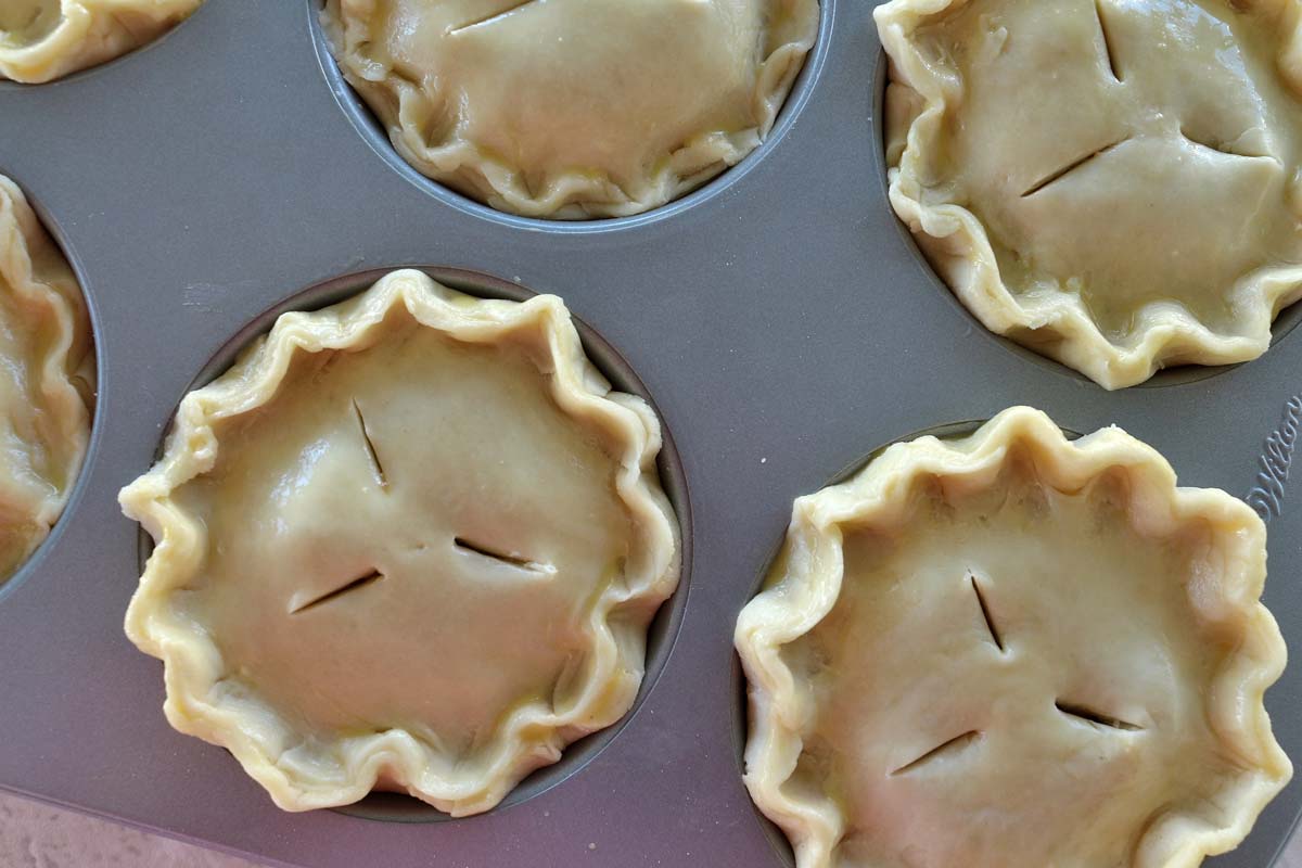 Individual unbaked pies with crimped edges assembled in a jumbo muffin pan.