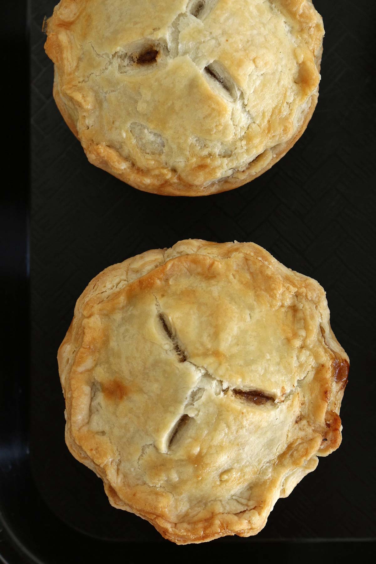 Two baked mini pies with crimped edges and 3 vents on a black background.